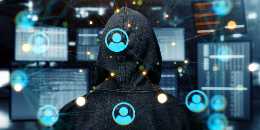 Criminal network threats depicted with person in hoodie in front of computers with data point connections overlaid