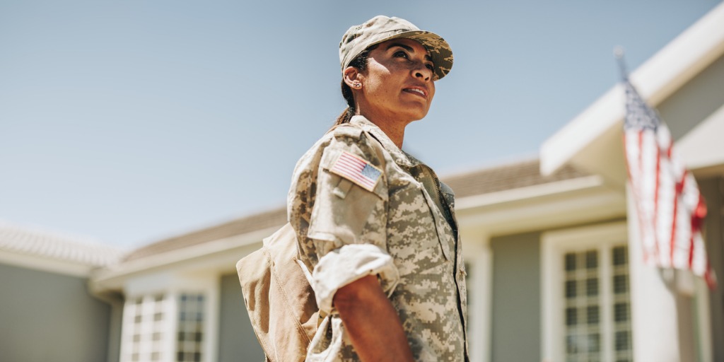 Courageous female soldier returning home with the American flag on the house behind her.